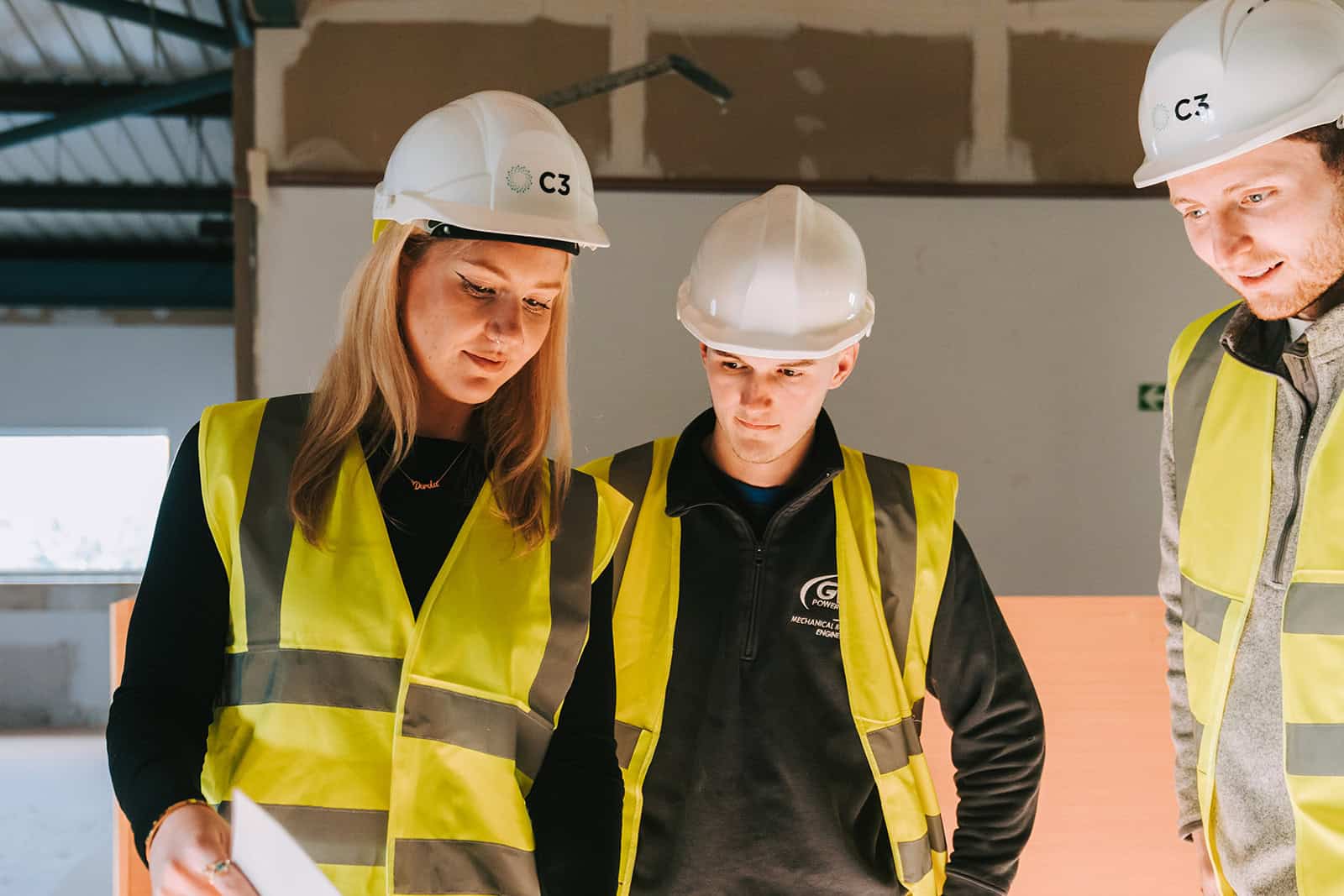 Three C3 Group sustainability consultants wearing hard hats and high vis vests, looking at blue prints